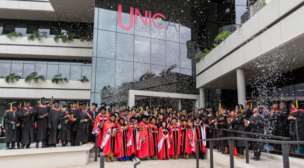 Graduates with graduation gowns and caps standing in front of Unicaf University in Zambia