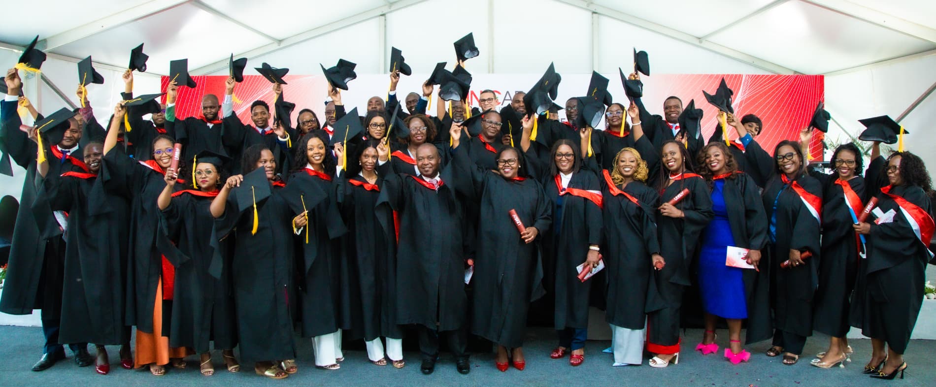 Smiling graduates wearing graduation gowns and holding up their graduation caps.
