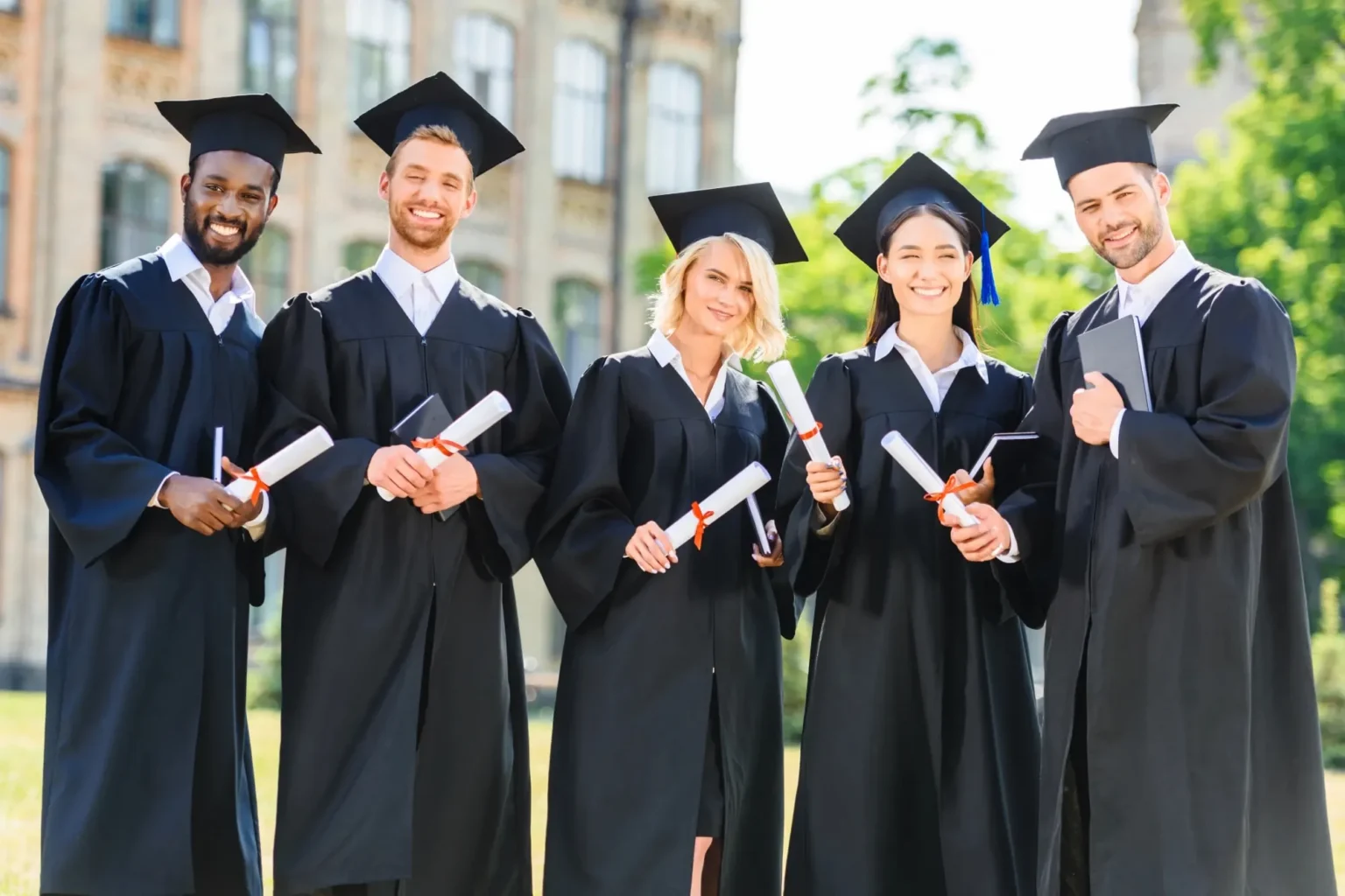 Smiling graduates wearing graduation gowns and caps, holding diploma.