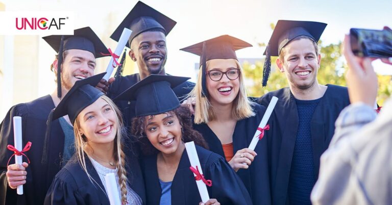 Smiling graduates wearing graduation gowns and caps, holding diplomas.